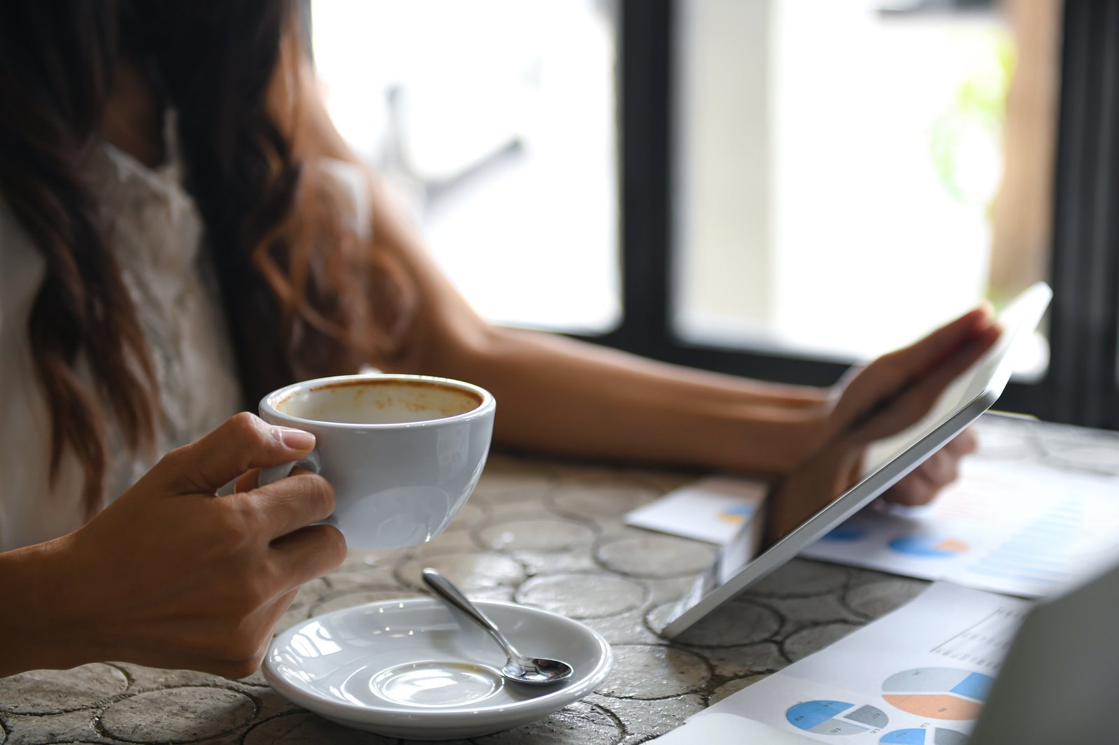 Female executive drink coffee and use tablet during break.She sat by the window in the office.